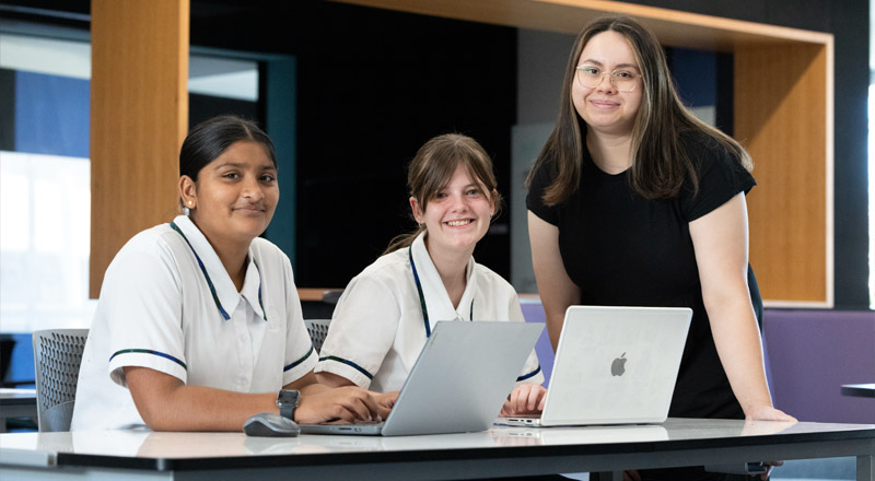 Two Nagle Catholic College students working on their laptop and being assisted by a teacher